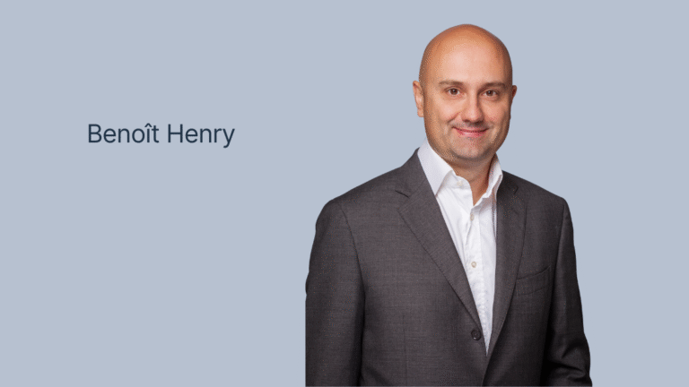 Porträt eines Mannes mit Glatze in einem dunklen Sakko und weißem Hemd vor einem einfarbigen hellblauen Hintergrund mit dem Text "Benoît Henry"