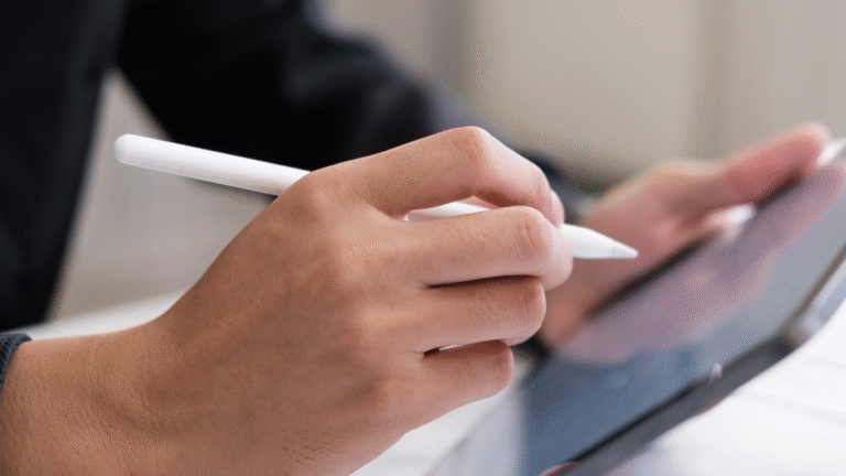 Hand hält einen weißen Stylus und bedient ein Tablet mit schwarzem Rahmen in einem hellen Innenraum