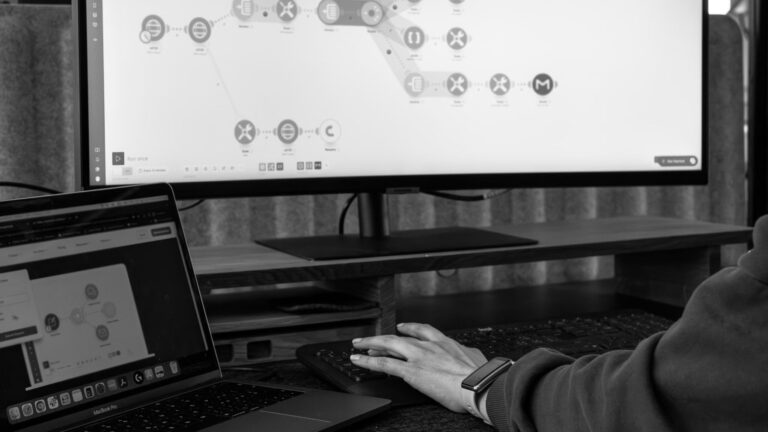 Nahaufnahme: Hand an der Maus, während digitale Prozesse auf Monitor dargestellt werden