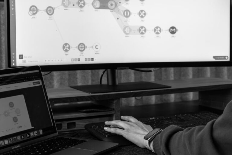 Nahaufnahme: Hand an der Maus, während digitale Prozesse auf Monitor dargestellt werden